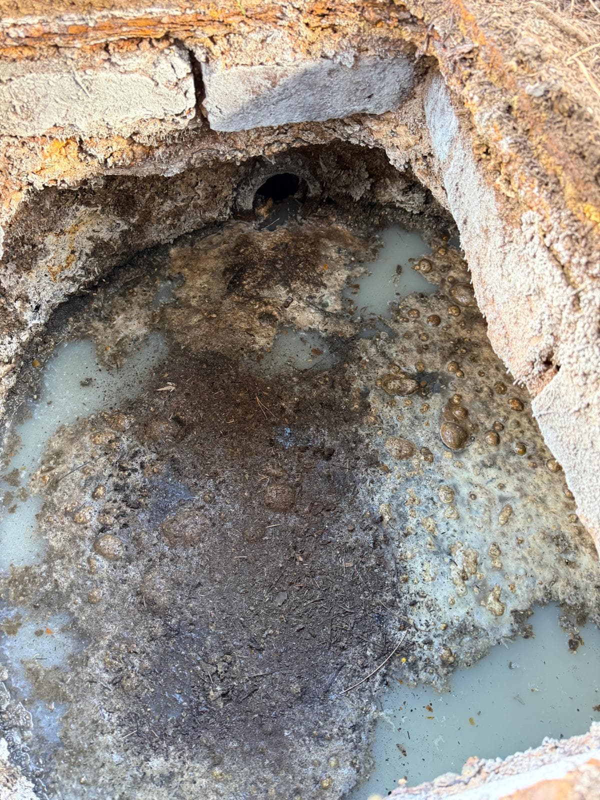 Masonry chamber interior showing a pipe opening, liquid and surface material