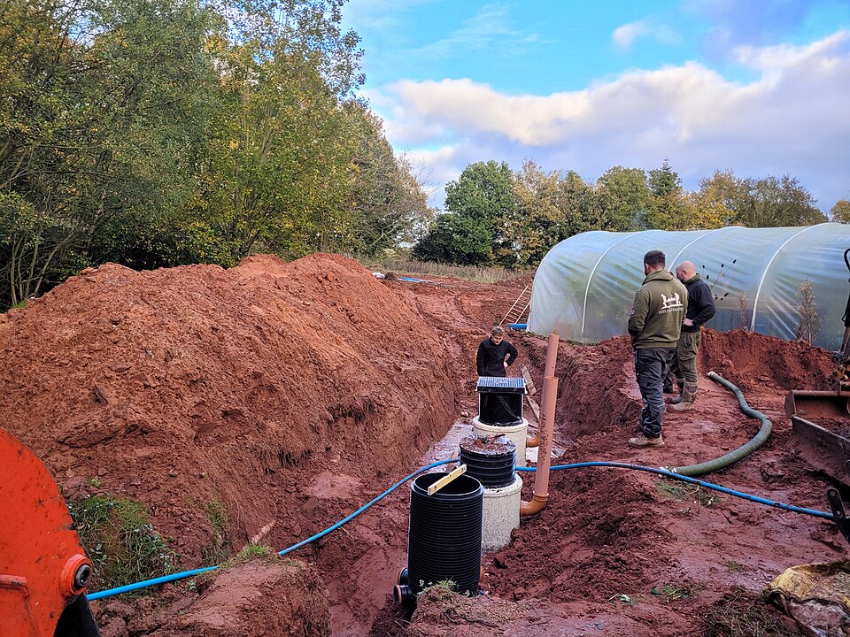 Reference photo showing tank access risers and connecting pipework during excavation at a separate installation