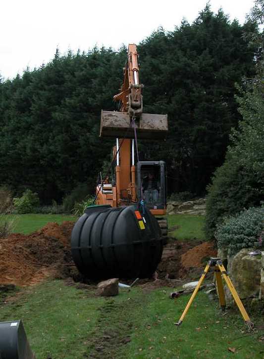 Third-party reference photograph of an excavator positioning a polyethylene septic tank